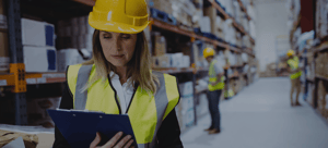 Banner for Routeique's blog on adopting supply chain technology. A woman is standing in a warehouse in a yellow hard hat, looking at a clipboard.